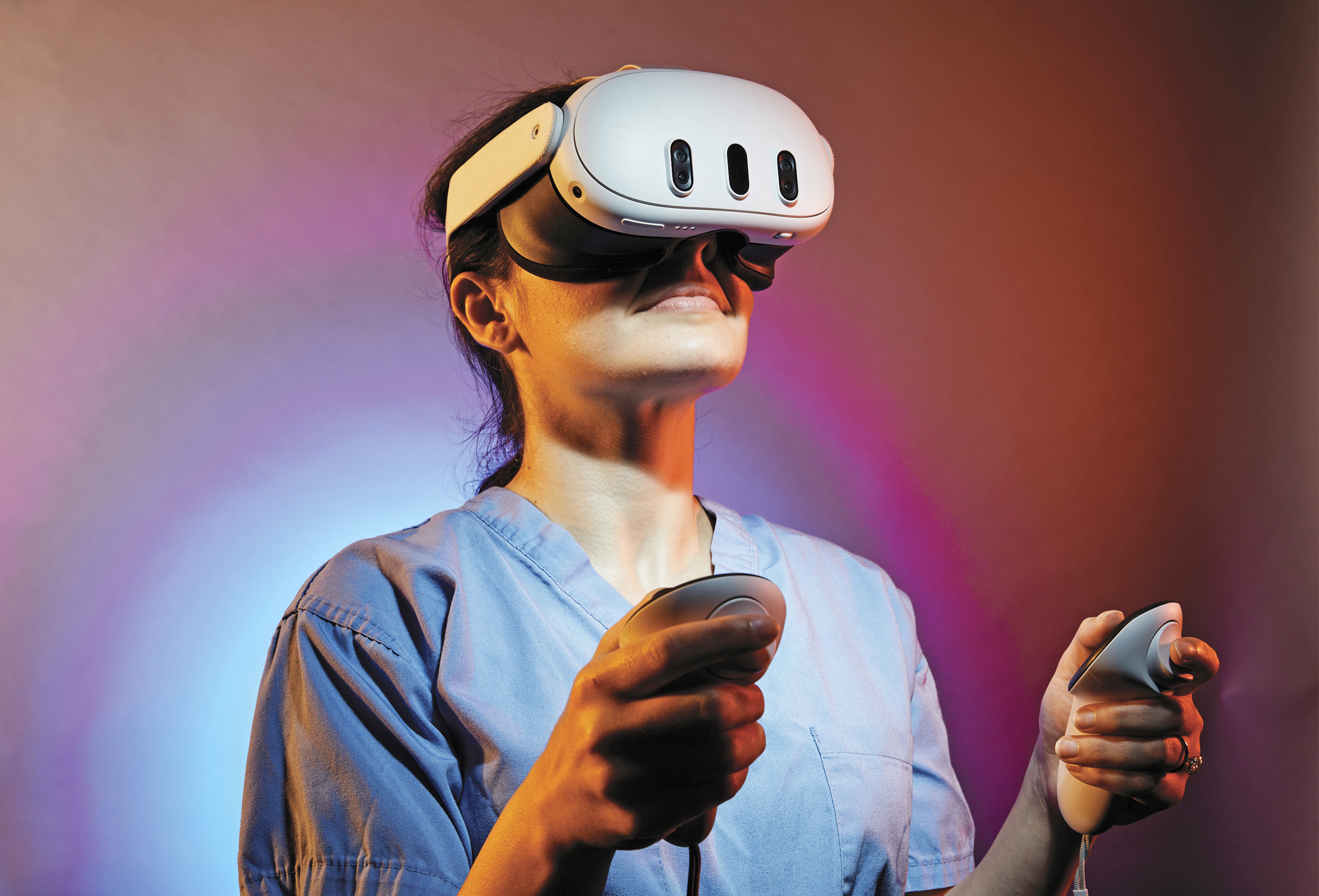 Female doctor in scrubs smiles while wearing virtual reality headset and holding controls.