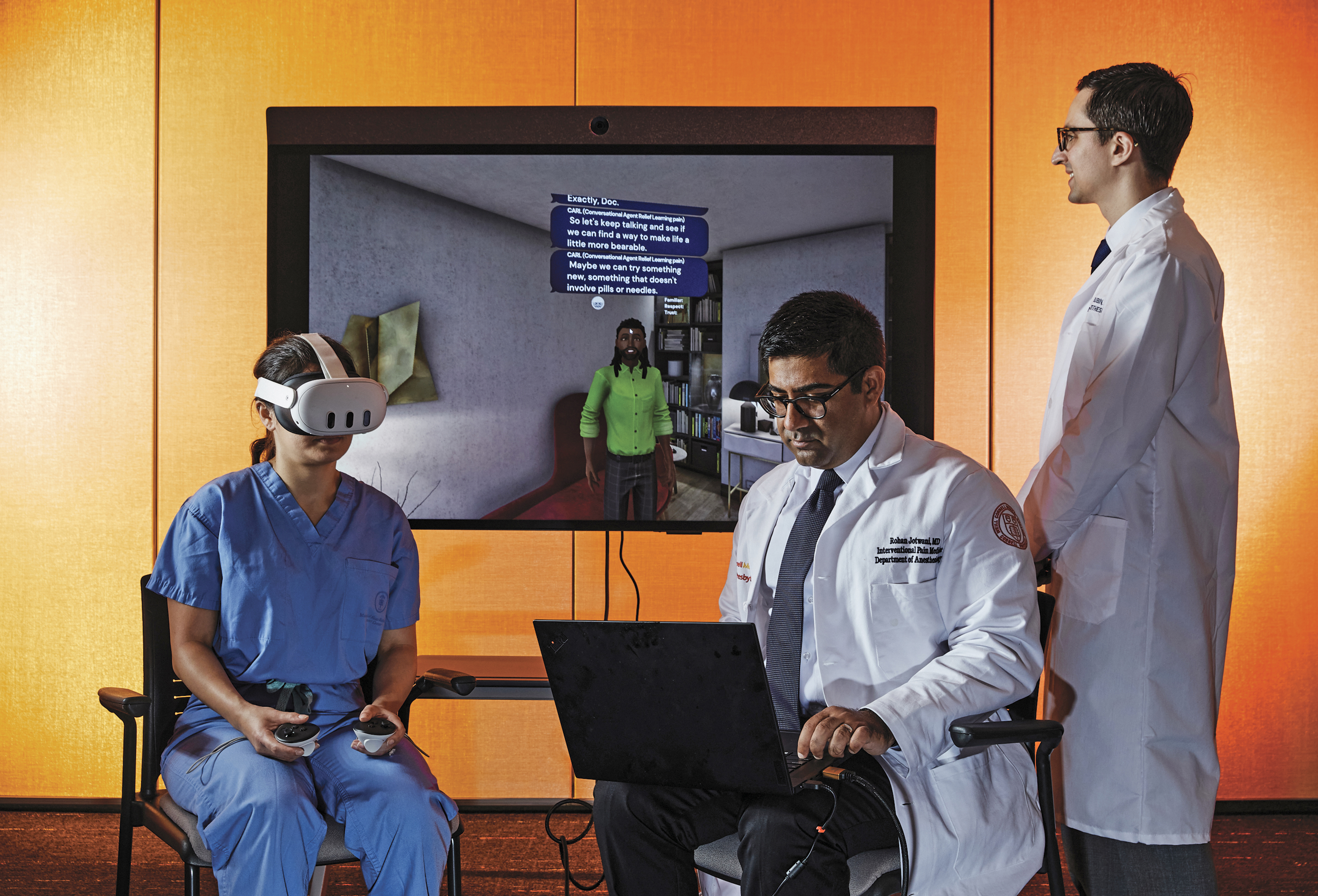 Female doctor in virtual reality headset demonstrates using an A.I. conversational agent while one male doctor in white coat operates the computer and another male doctor in a white coat looks on.