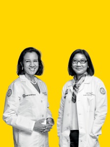 Black and white photos of middle-aged smiling South Asian woman in white doctor’s coat with shoulder-length hair partially facing middle-aged smiling East Asian woman in glasses and white doctor’s coat with shoulder-length hair, transposed onto solid, bright yellow background. They are (on left) Dr. Renuka Gupta, and (on right) Dr. Judy Tung.