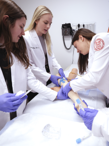 Three students practice inserting an intravenous catheter.