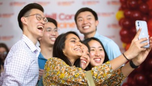 Three East Asian male medical students gather behind one South Asian and two East Asian medical students, all smiling for a group selfie. 