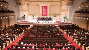  Interior of Carnegie Hall auditorium with seated medical college graduates in mortarboards and red and green robes, as well as other attendees, shown from above at Commencement.