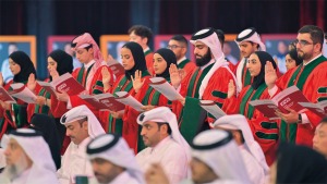Students in red, green and black graduation robes and mortarboards holding their right hands up