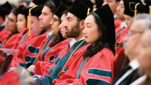 Seated students in red, green and black graduation robes and mortarboards