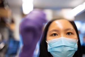 Closeup of young, East Asian woman with shoulder length black hair wearing blue face mask examining slide. 